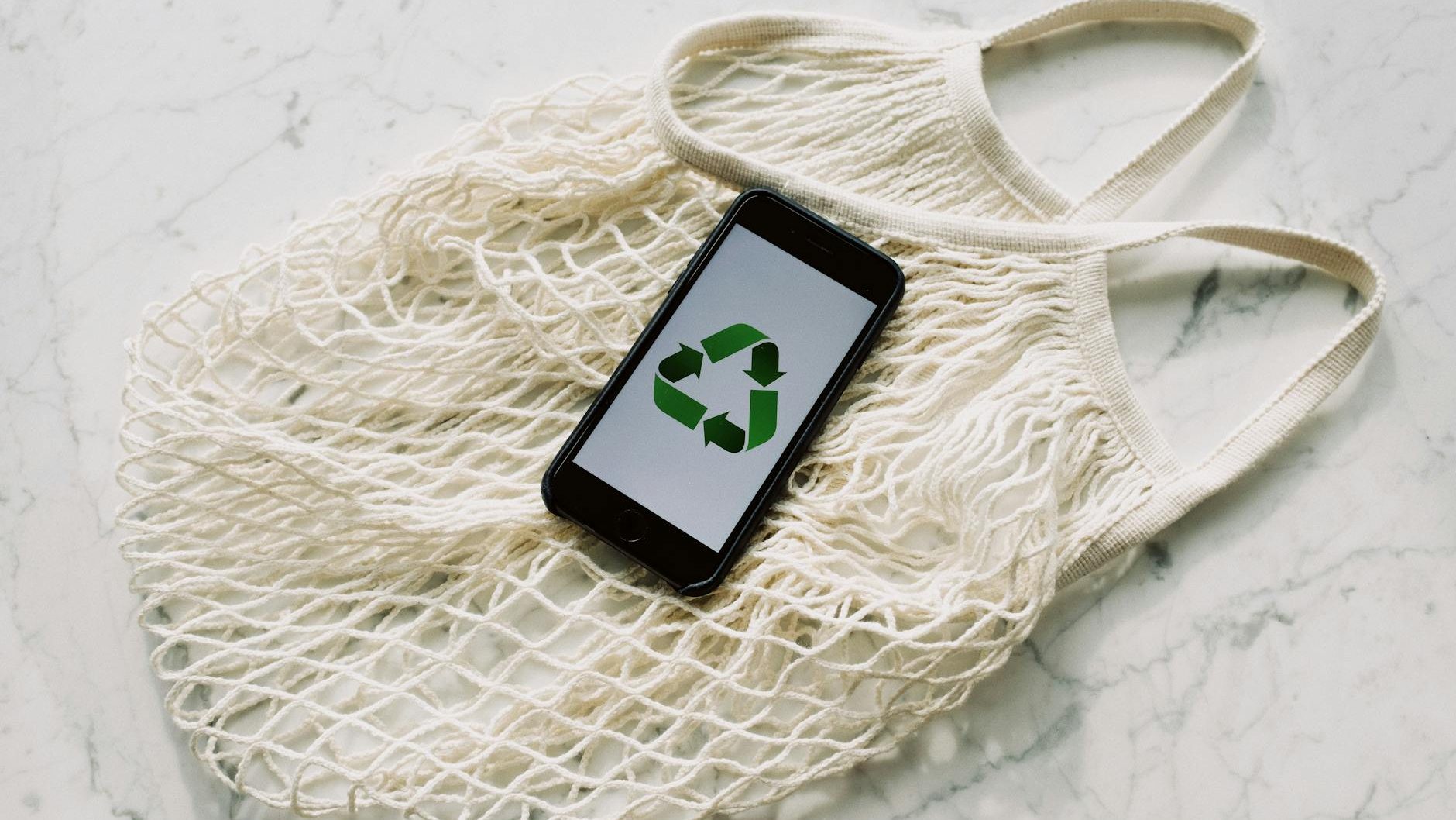 A phone with a recycling graphic on the screen sits on top of a reusable bag