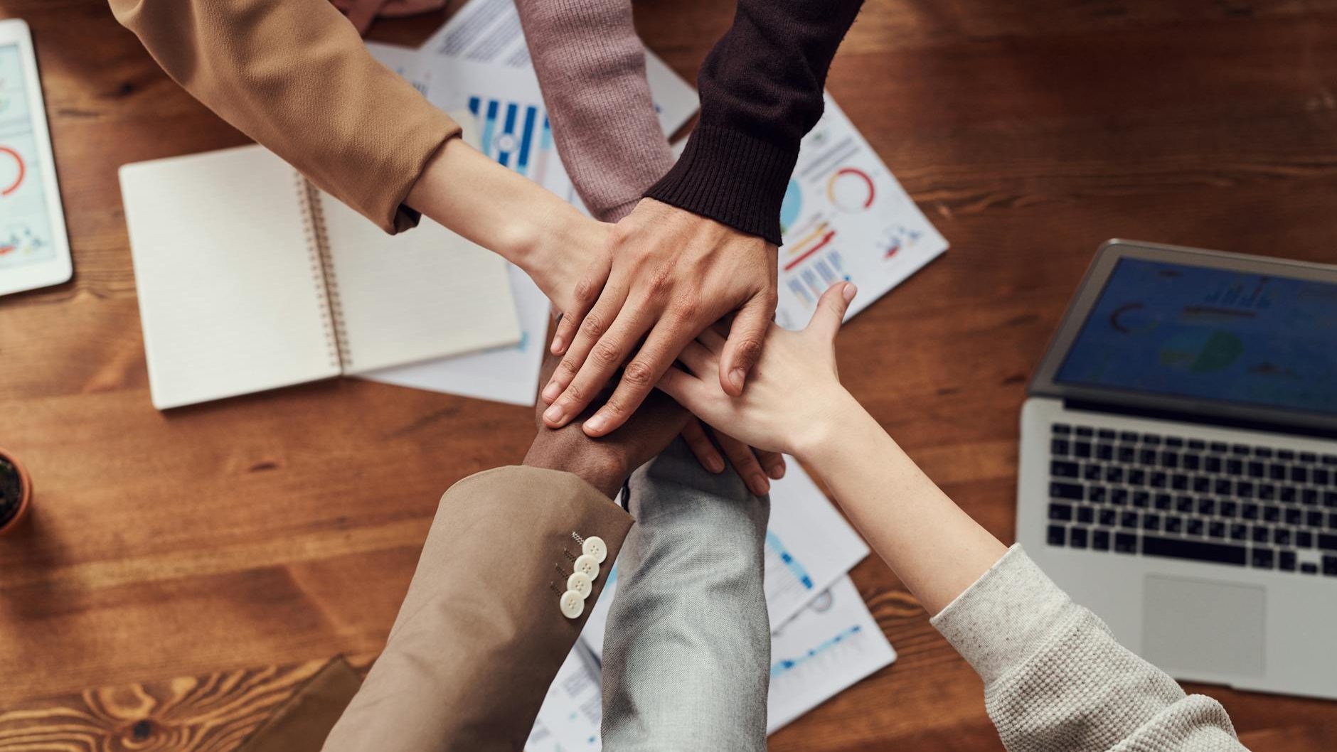 A joining of hands centered over work papers and a laptop