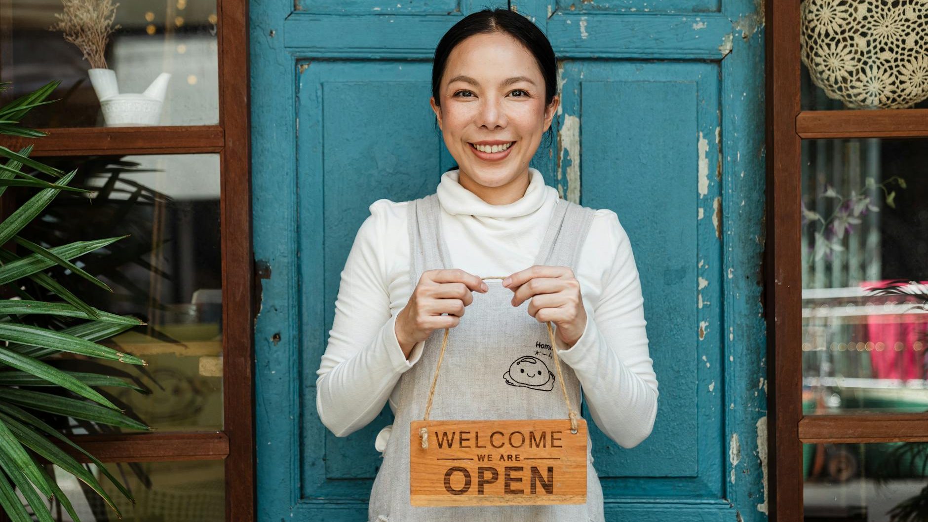 A women standing in front of a door holding an Open sign