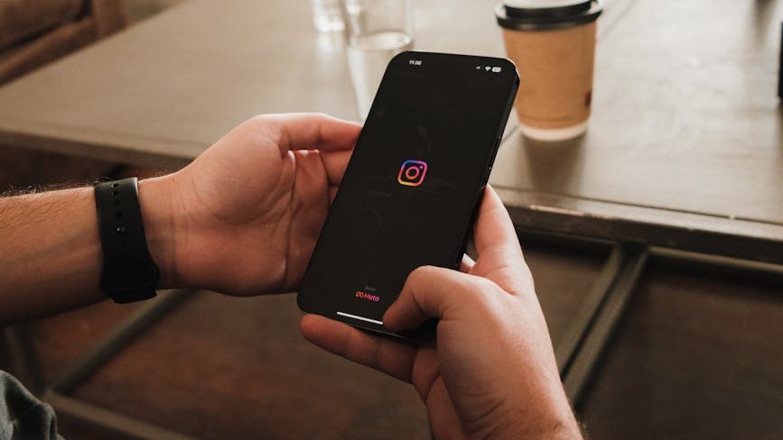 Hands holding a phone with a black screen and the Instagram logo on it