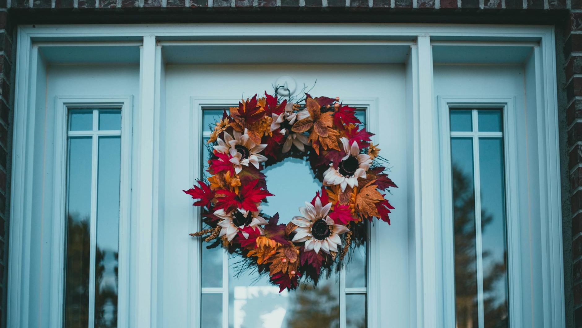 A wreath of fall leaves hangs on a white door