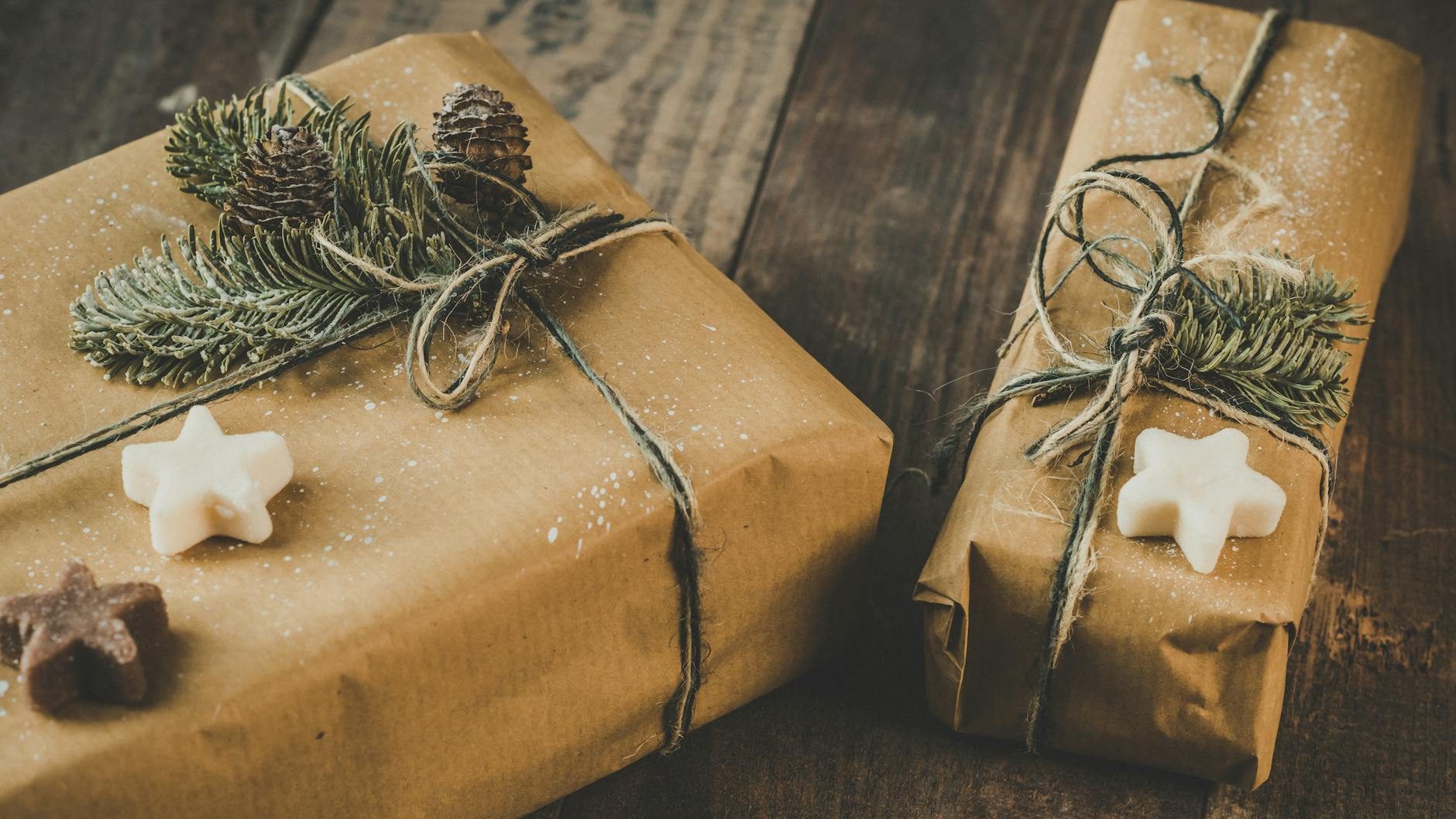 Two packages wrapped in brown paper and twine with pine branches and pinecones on top