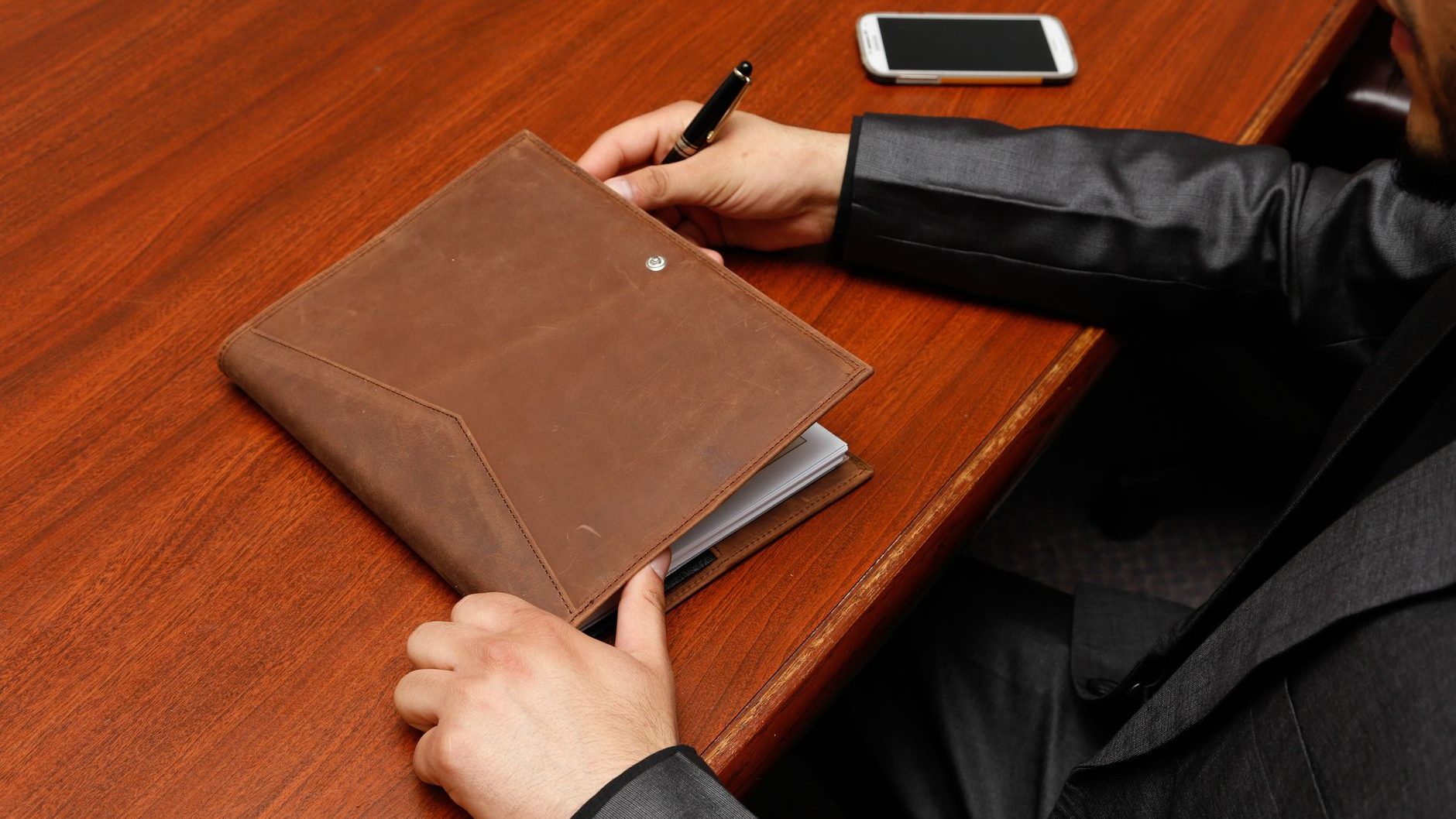 A leather-bound notebook on a desk with a phone next to it